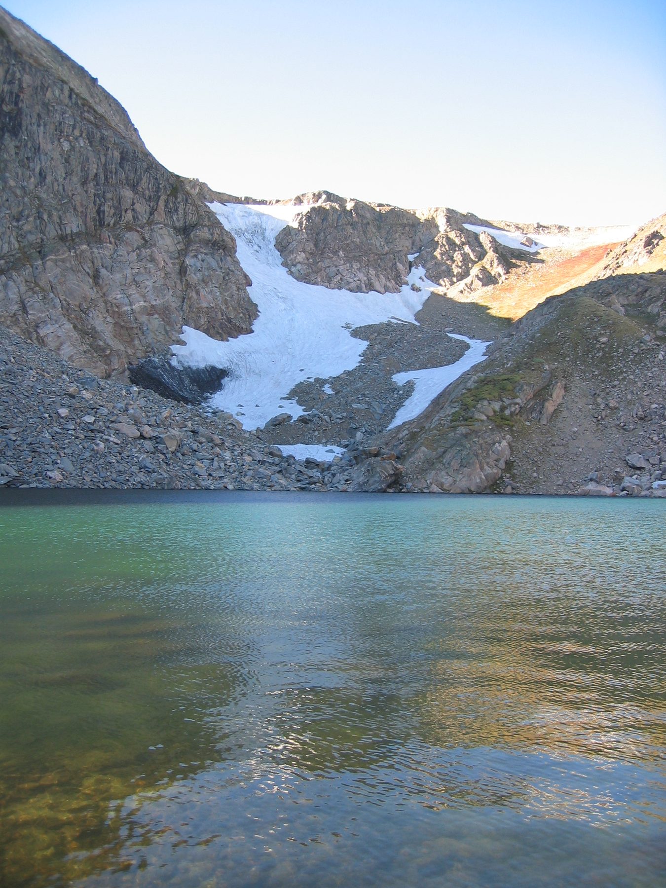 Turquoise alpine lake below a snowfield